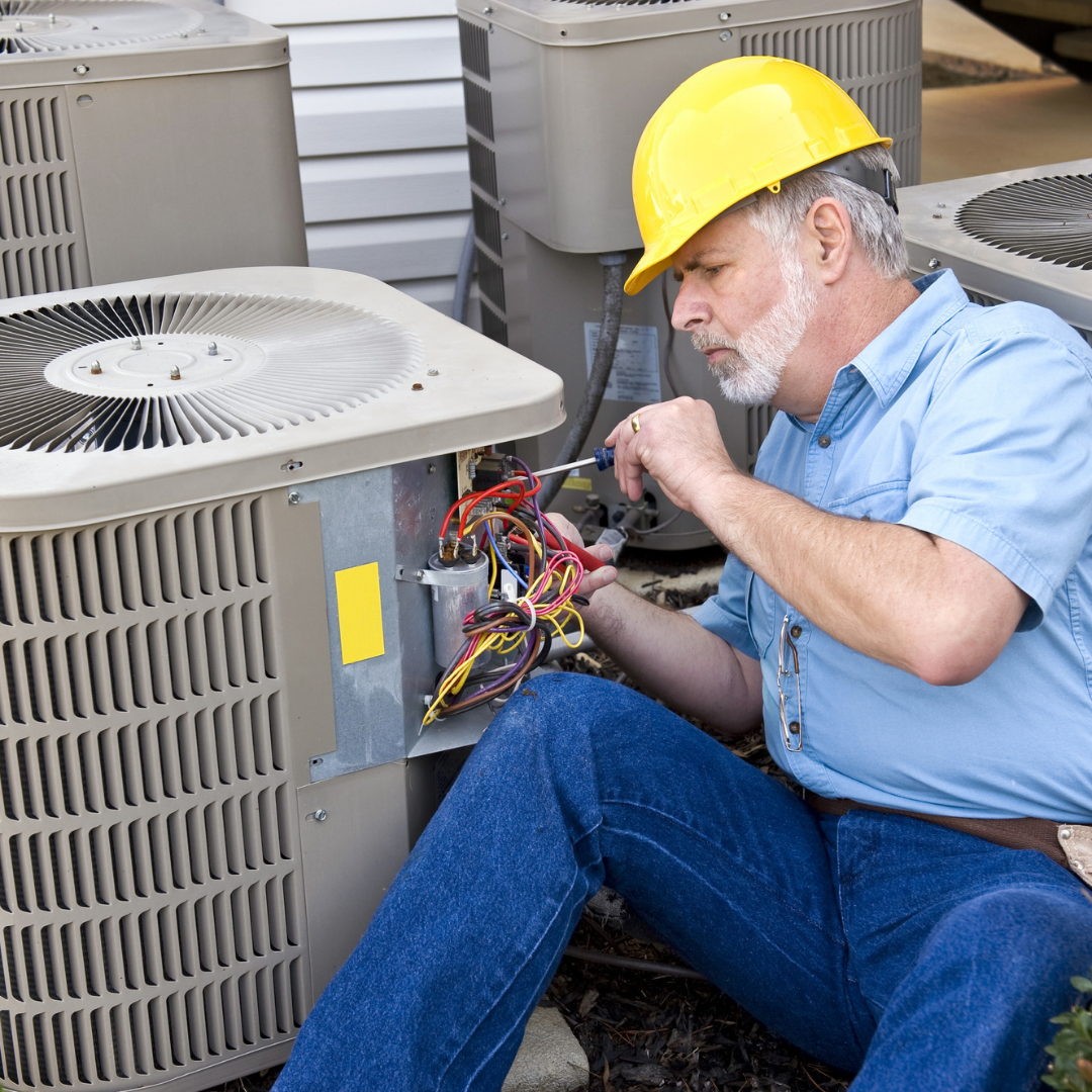 technician wearing a hard hat repairing wiring on an outdoor residential air conditioning unit