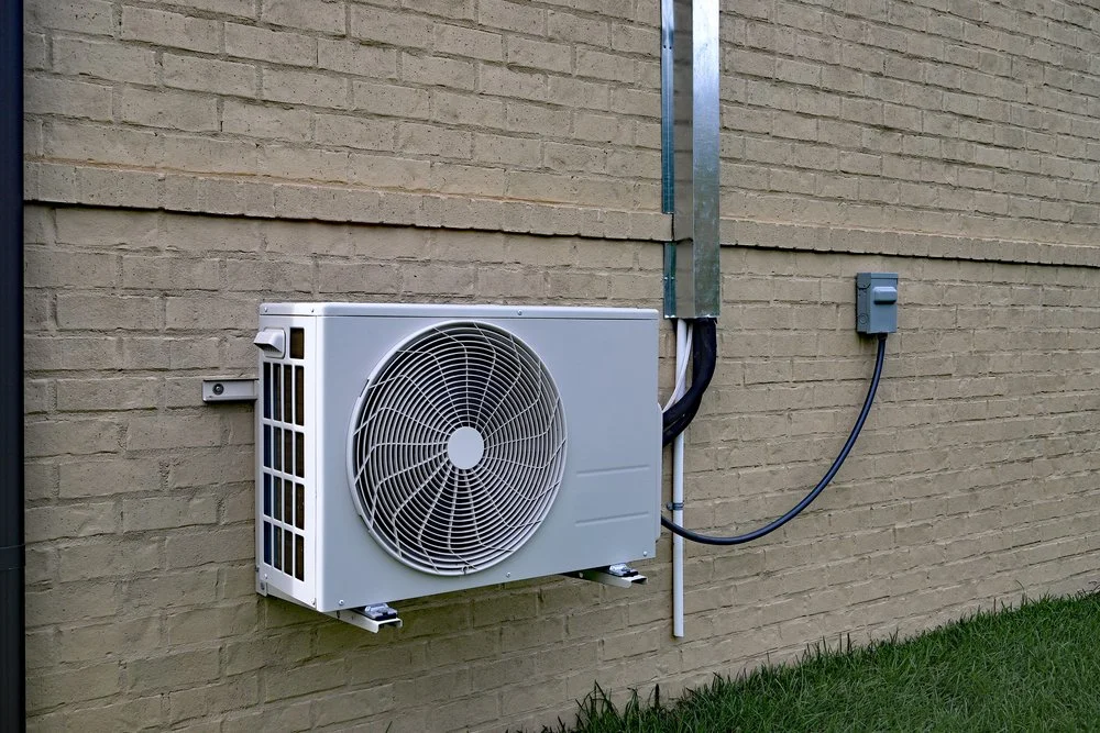 outdoor heat pump unit mounted on a brick wall with connected electrical and refrigerant lines