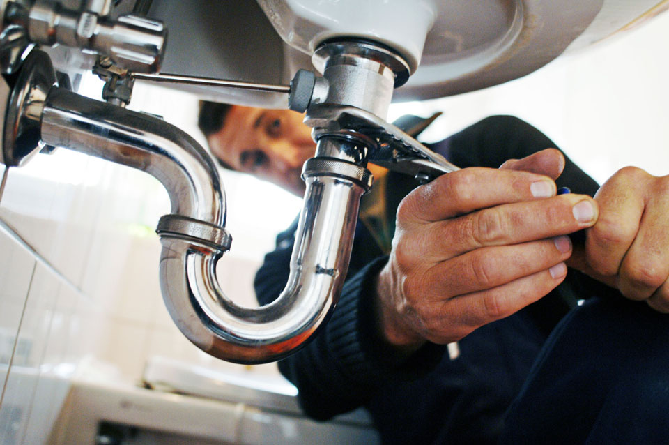Person using a wrench to tighten metal drain pipes beneath a bathroom sink