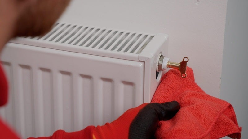 person using a bleed key to release air from a wall-mounted home radiator with a cloth underneath