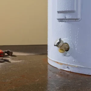 Leaking water heater tank on basement floor indicating need for replacement or plumbing repair