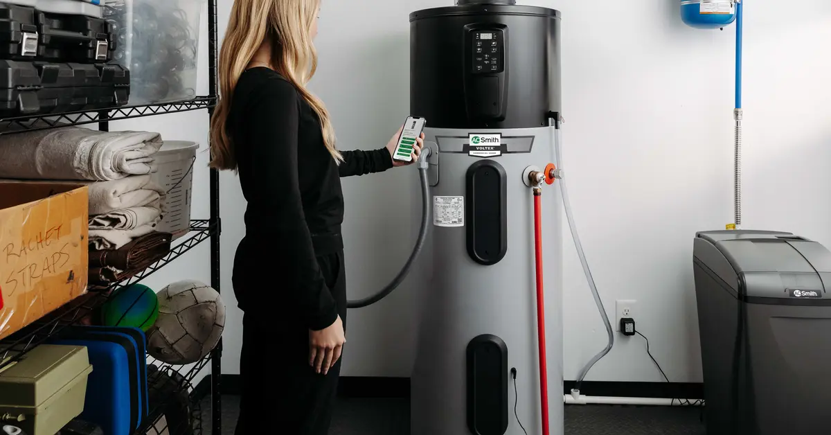 Person standing in a home utility room beside a heat pump water heater and connected plumbing equipment