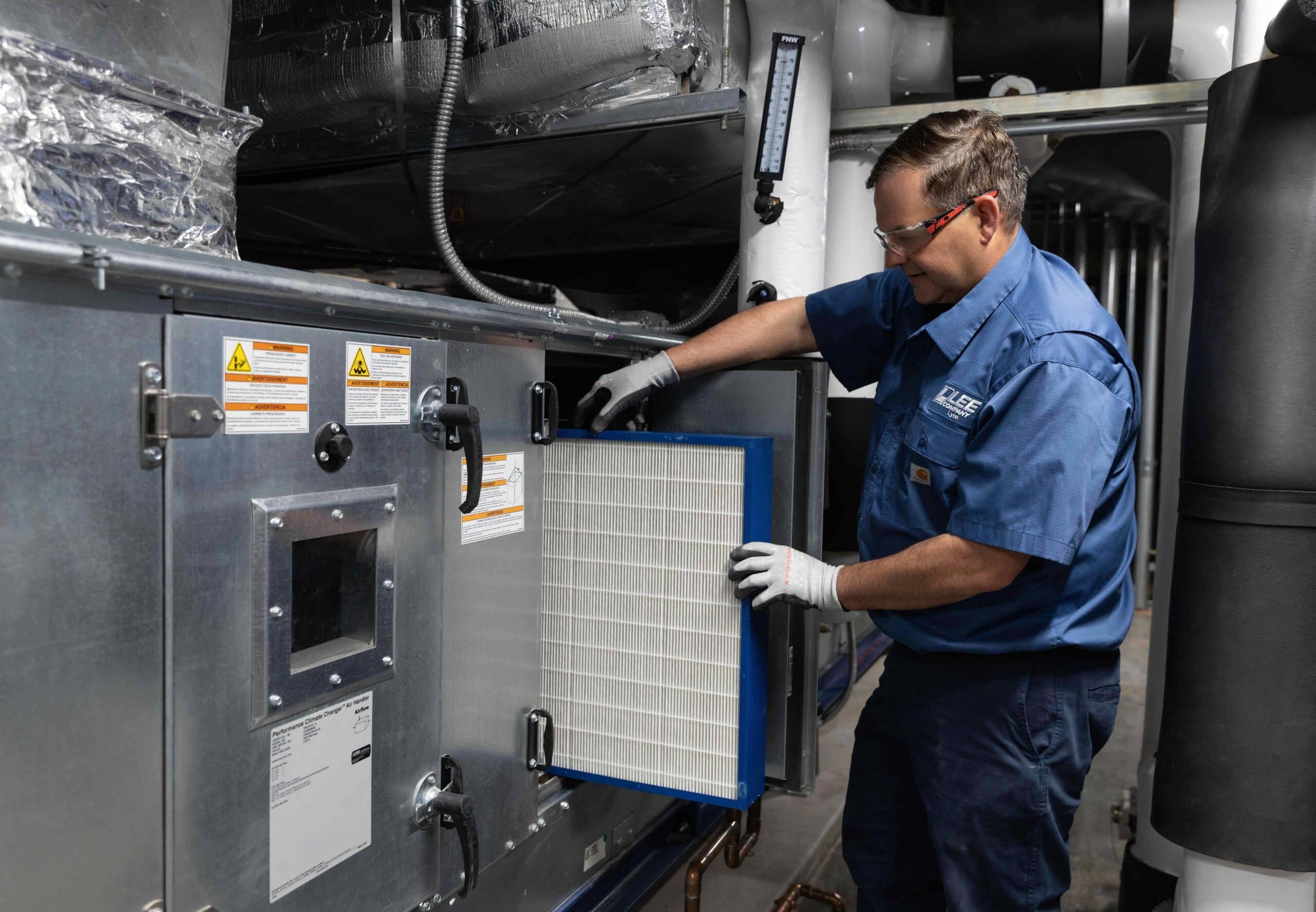 Technician wearing safety gloves installs an air filter into a large HVAC unit inside a mechanical room