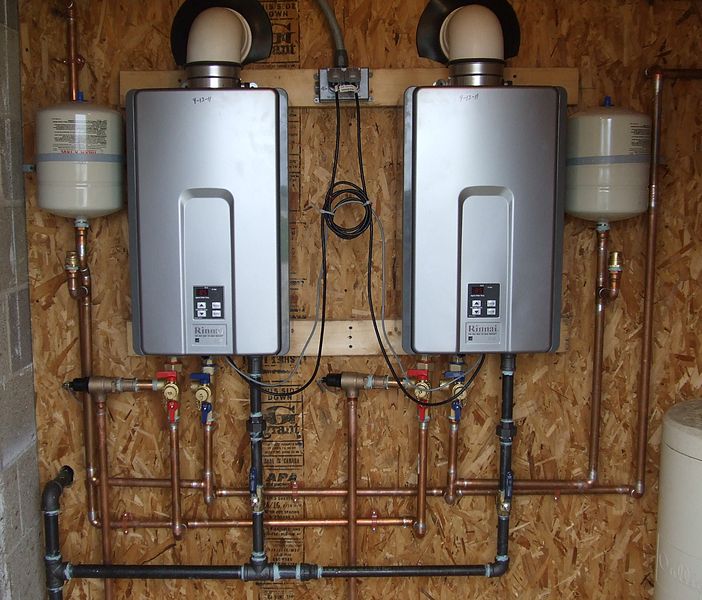 Two wall-mounted tankless water heaters connected by copper pipes in a residential utility room
